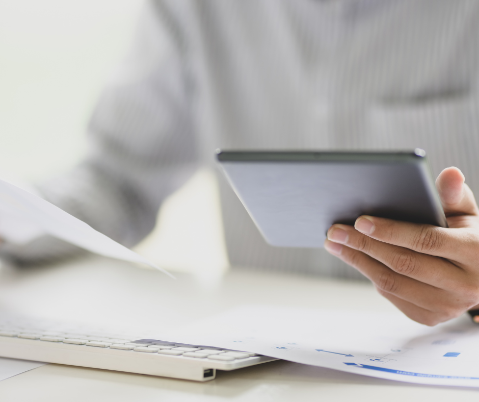 Man with gray button-down shirt holding a note book looking at a papers.