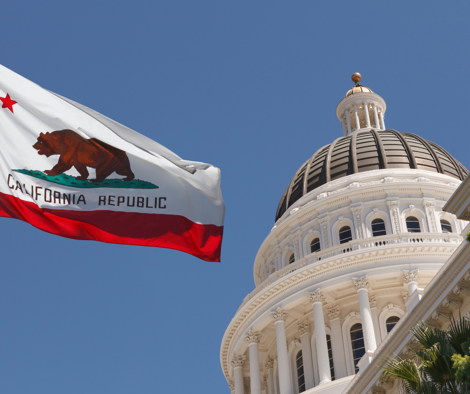 California flag flying next to government building in front of a blue sky.