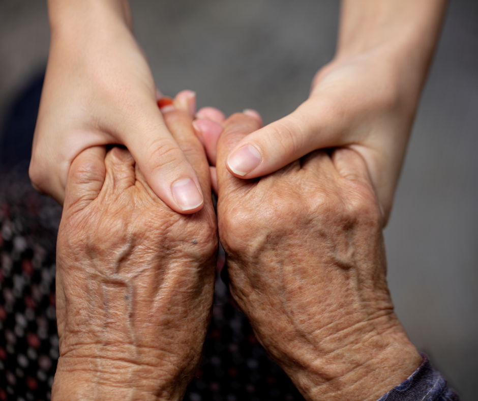 Two pairs of hands, one from a younger person and one from an older person, hold each other.