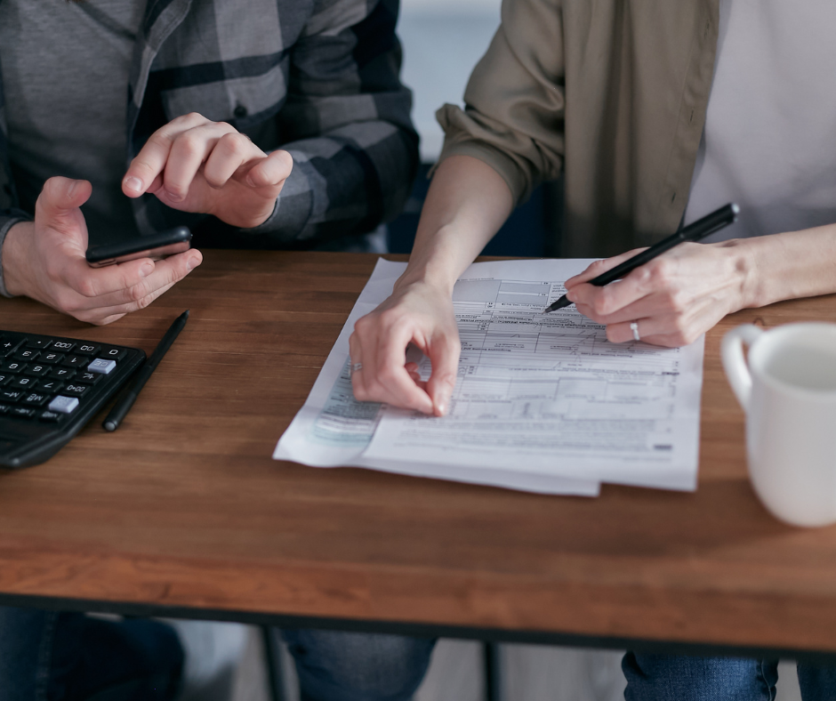 2 people calculating taxes with a calculator and documents on top of a wooden table.