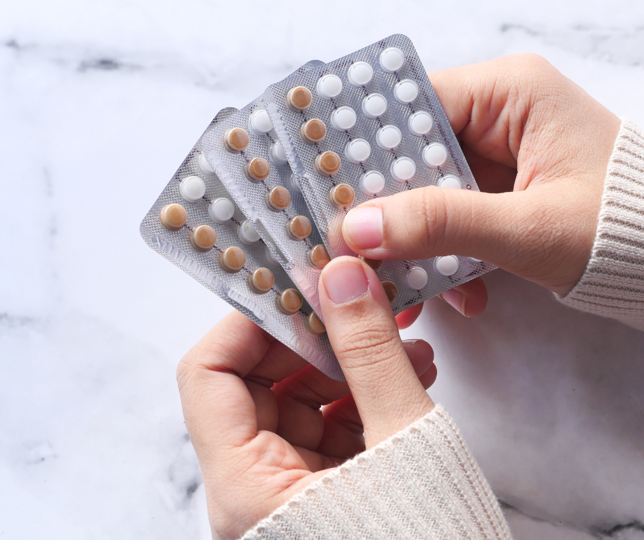 Women wearing sweater holding 3 pill packet with white and brown bills inside.