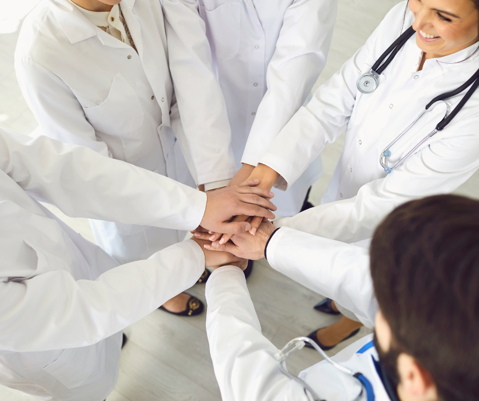 A group of people in lab coats have their hands placed on top of each other in the middle of a circle