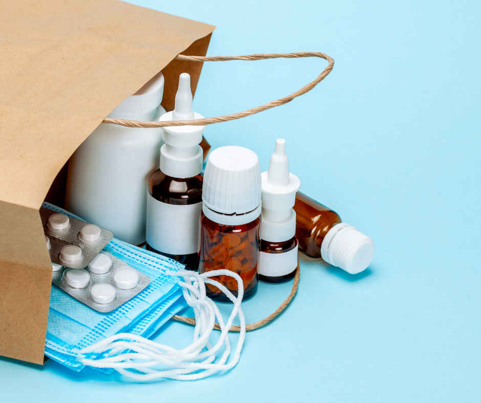 Paper bag on its side filled with medication, masks, eye drops, and pill packets.