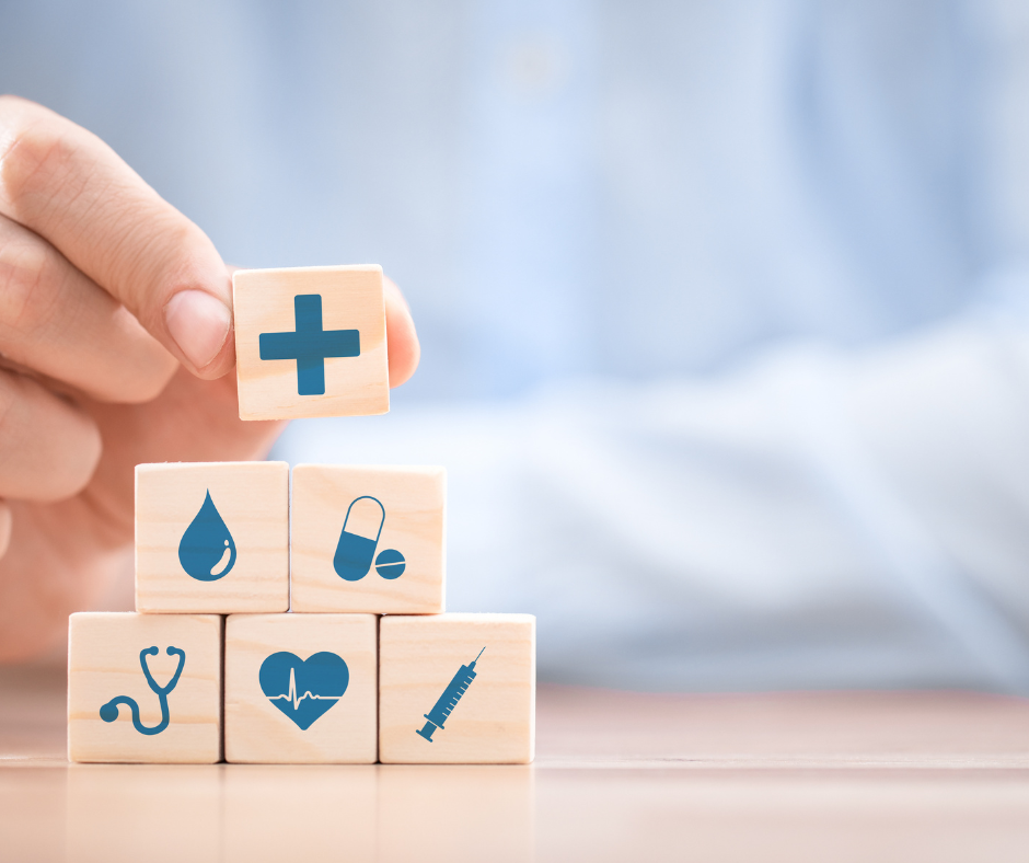 Person stacking a cube with a medical cross sigin on top of 5 cubes with varying medical symbols similar to a pyramid style.