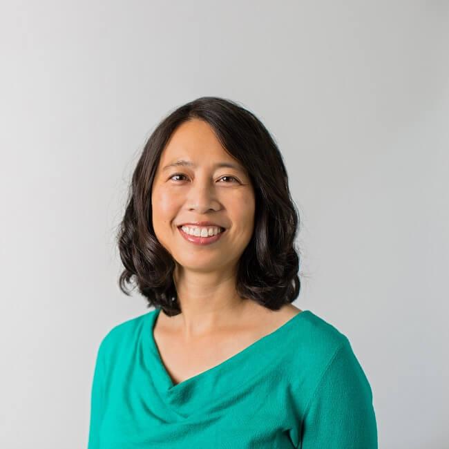 Smiling asian woman with black wavy hair that goes to her shoulders wearing a teal blouse.