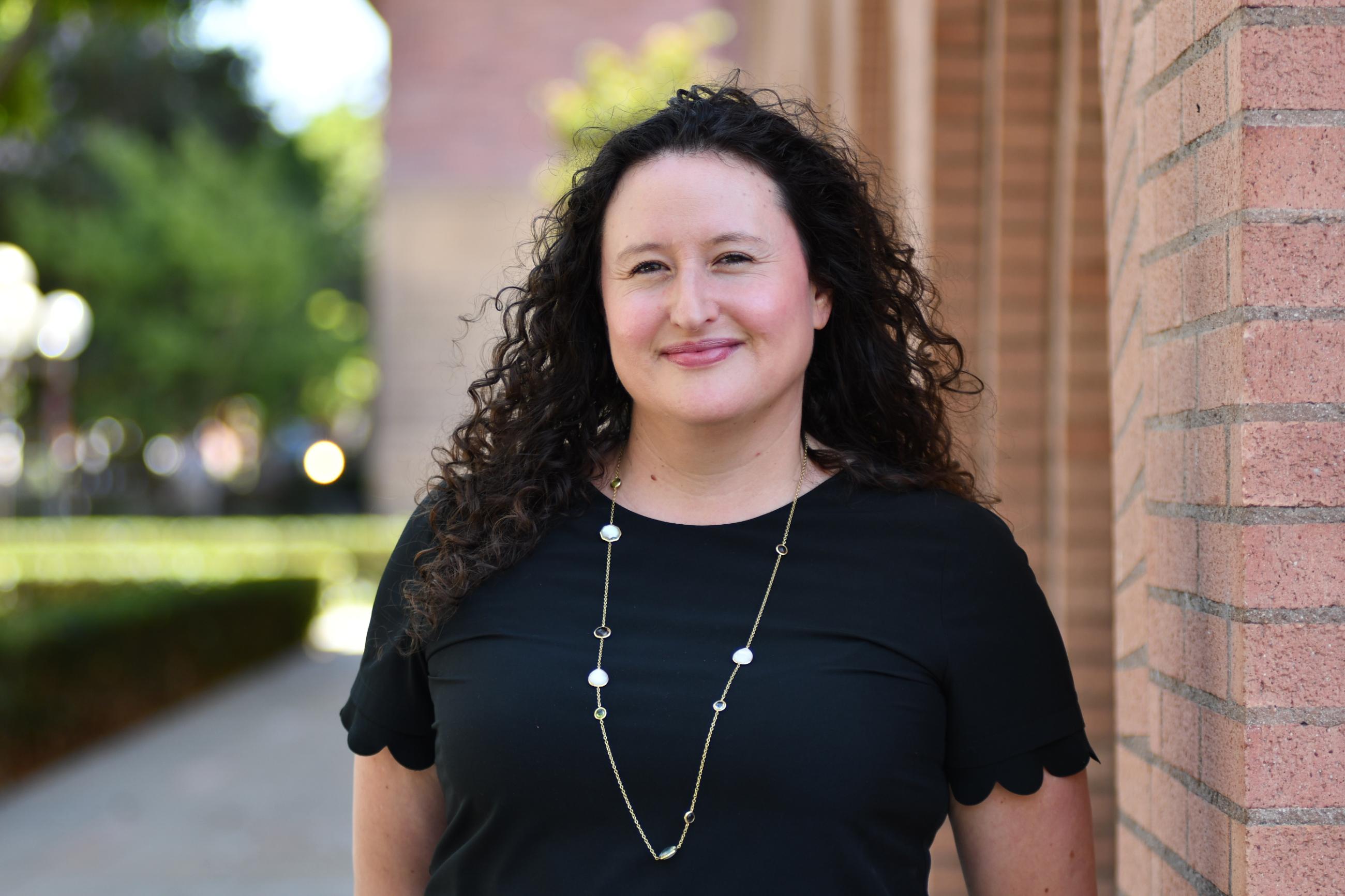Woman with brown curly hair in front of a brick wall